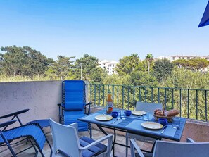 A dining area with a table set for two, chairs, and a view of a residential area with trees and buildings. - L'Annonciade by Interhome (Port Cogolin)