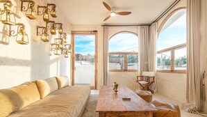 Ein Zimmer mit einer Couch, einem Holztisch, Lederhocker, einem Regiestuhl und wandmontierten Laternen.