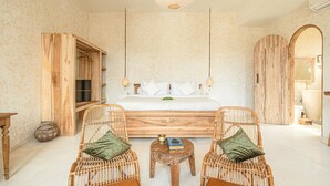 Ein geräumiges Schlafzimmer mit einem großen Bett, zwei Korbstühlen, einem kleinen Holztisch und einem Kleiderschrank.