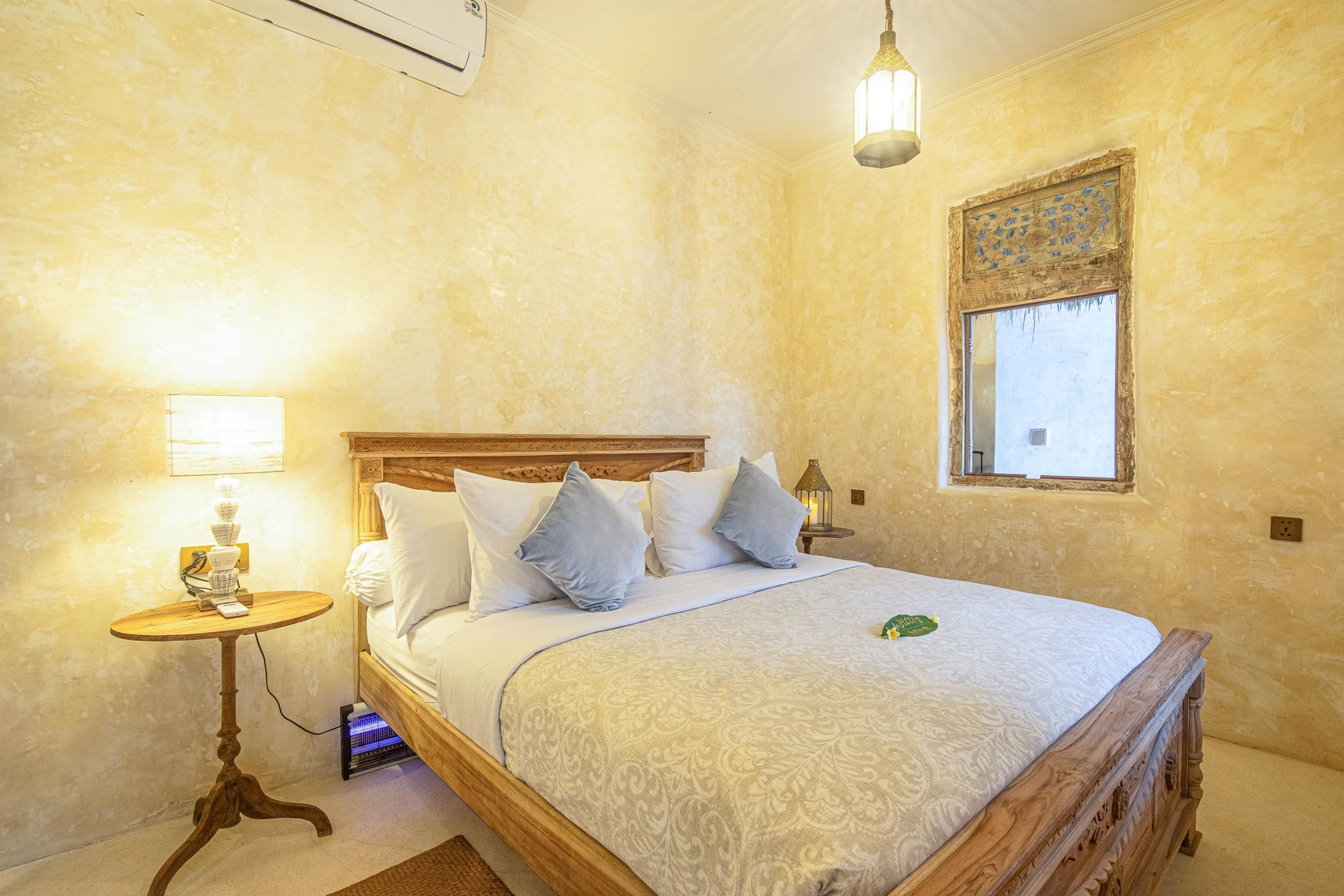 A bedroom with a wooden bed, white bedding, a bedside lamp, and a window with a decorative frame.