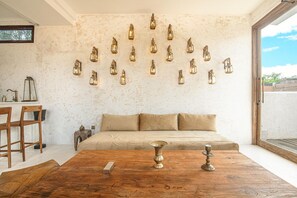 Quarto com sofá, cadeiras de madeira, mesa de centro com castiçal de latão e luminárias fixadas na parede.