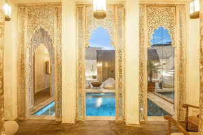 A luxurious indoor pool area with ornate columns and a clear view of the outside. - Stylish Villa Uluwatu Enclosed Living AC (Pecatu)