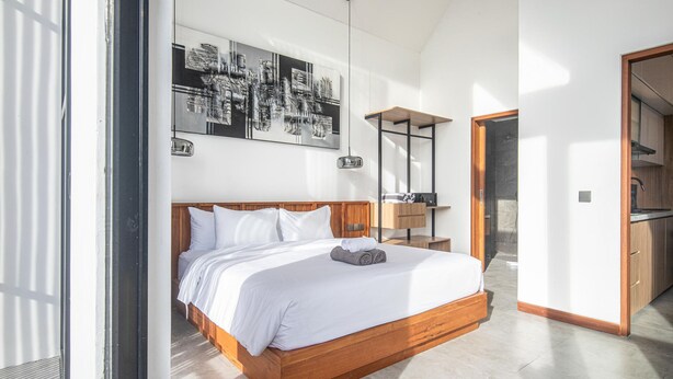 Une chambre à coucher moderne avec un grand lit, une tête de lit en bois, une table de chevet, une lampe suspendue et un grand tableau abstrait accroché au mur.