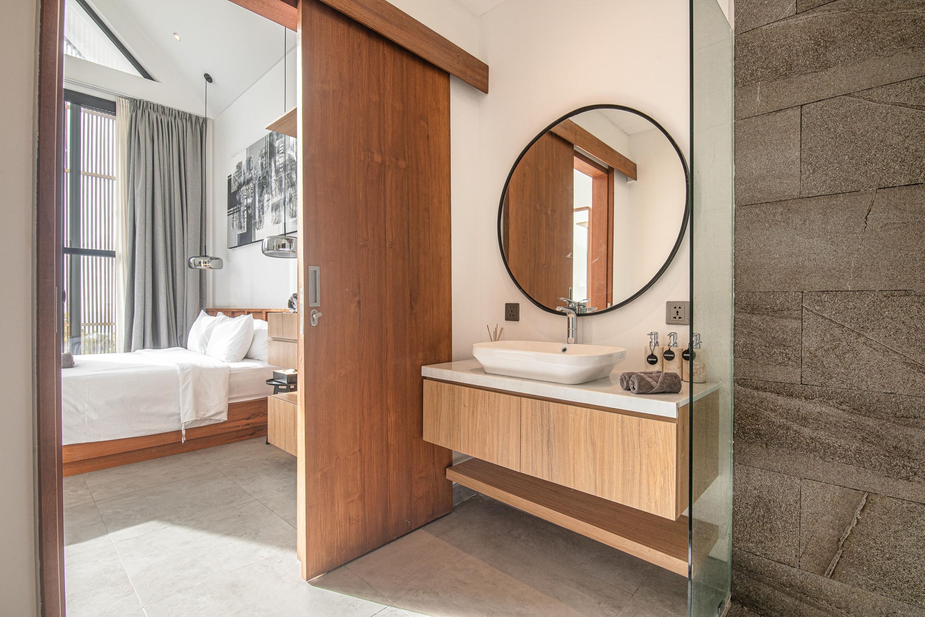 A modern bathroom with a wooden vanity, a round mirror, and a white sink.