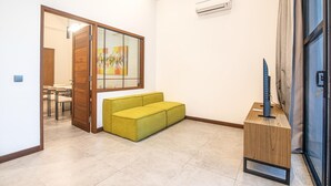 Une pièce avec un canapé vert, un meuble en bois et une porte donnant sur un autre espace.