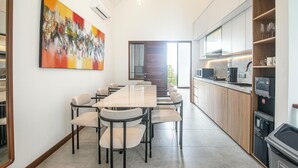 Une cuisine moderne avec une longue table à manger et des chaises, une grande peinture abstraite et une vue à travers une porte vitrée.