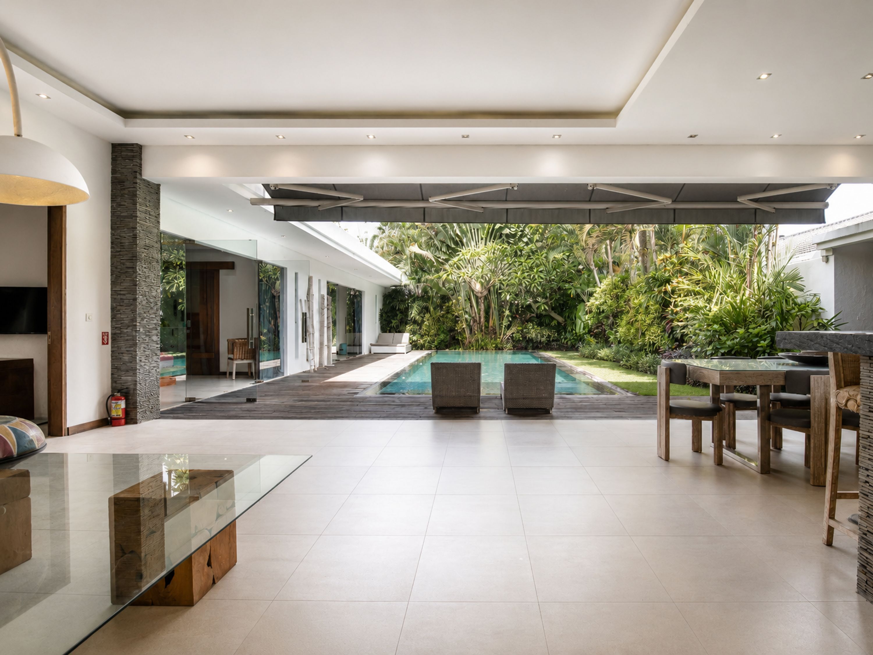A modern outdoor living area with a pool, seating, and a glass table.
