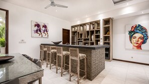 A modern kitchen with a bar area, wooden chairs, and a dining table. - Splendid Villa 3Br Center Seminyak (Keroboken Kelod)