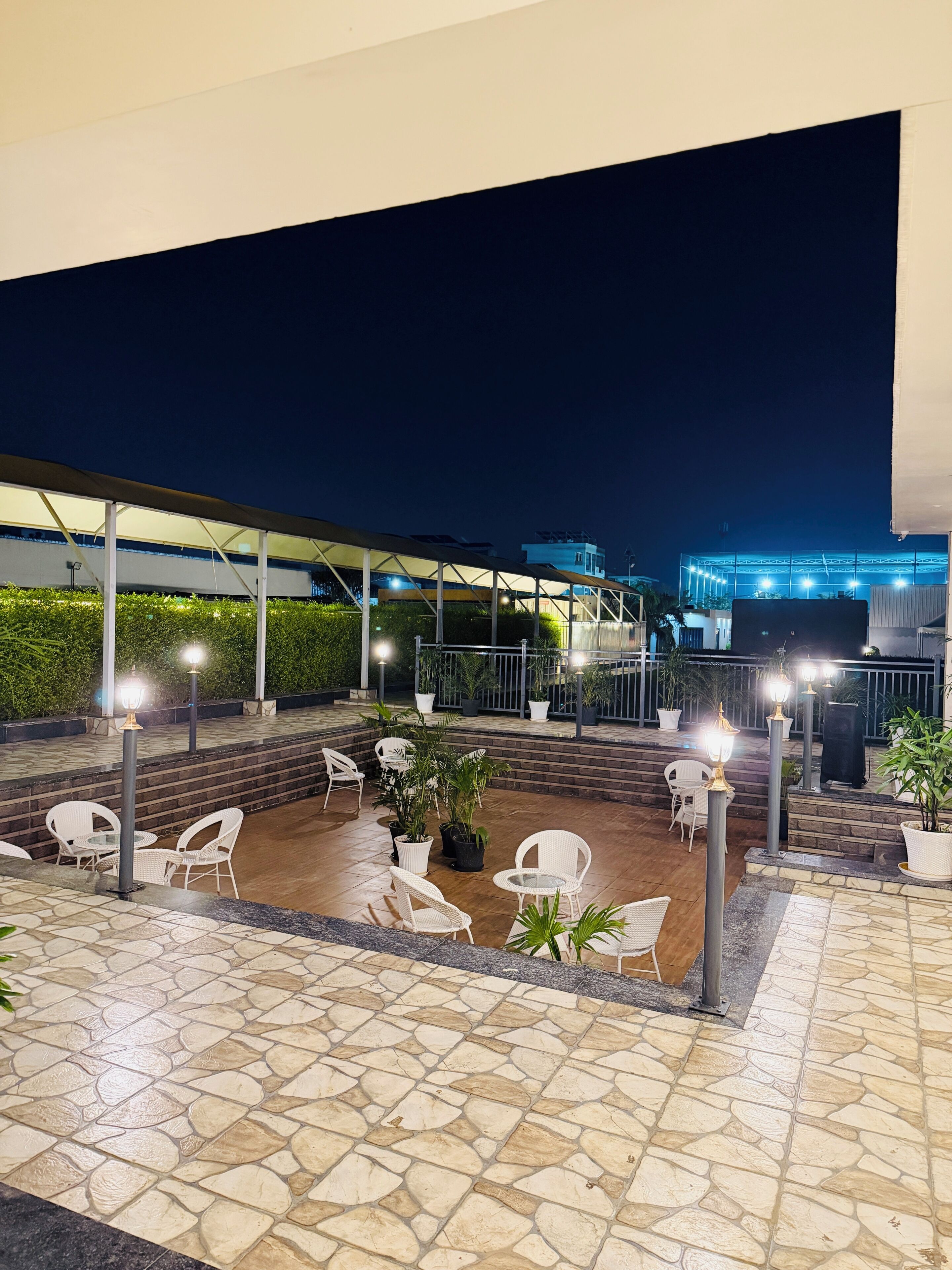 An outdoor patio area with stone flooring, white wicker furniture, and potted plants.