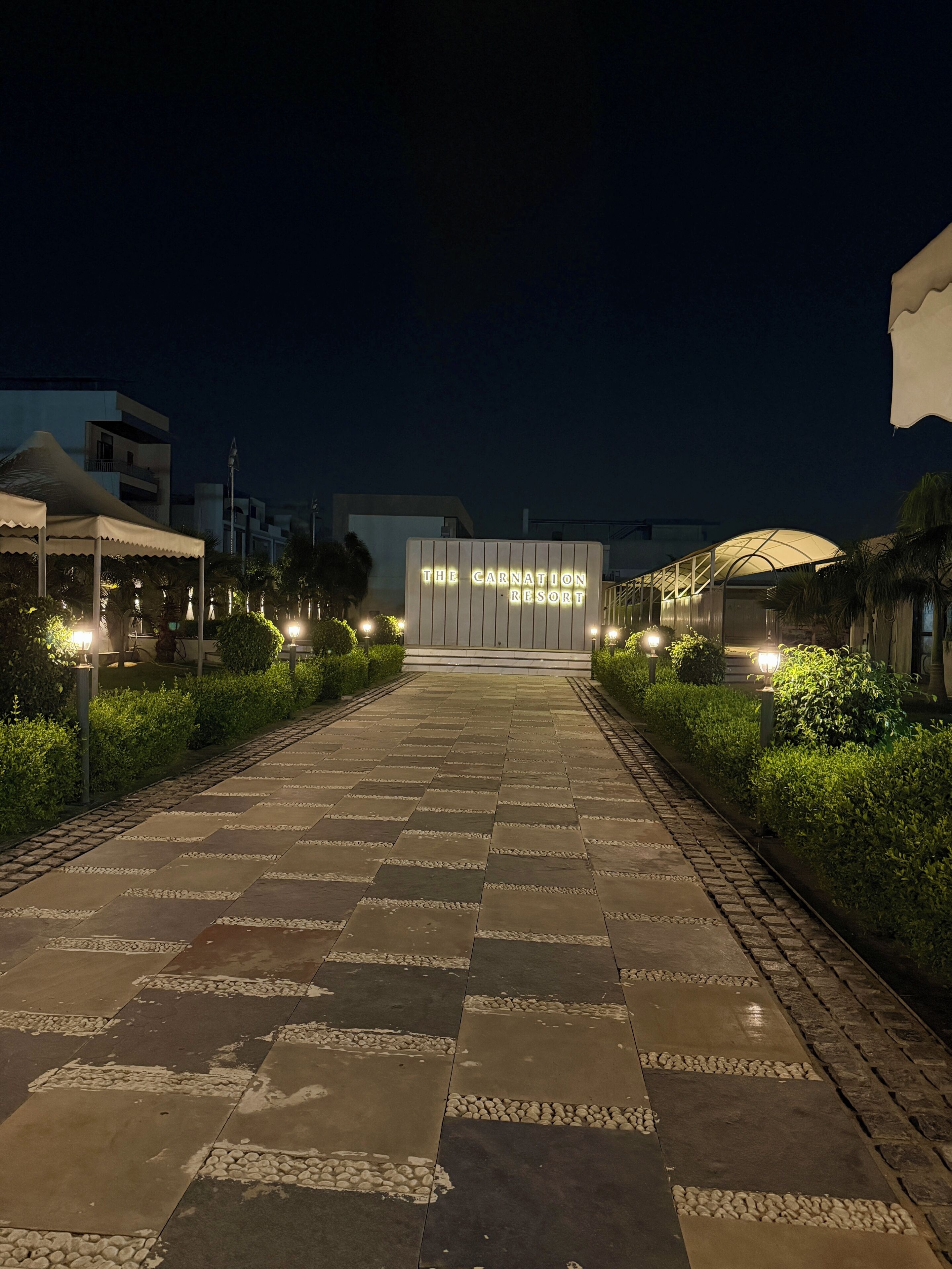 Un chemin pavé mène à un bâtiment dont l’enseigne lumineuse indique : « The Carnation Resort ».