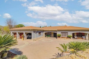 A two-story house with a covered driveway, a garage, and a patio area with seating. - Aaybee Recreational Place (Midrand)
