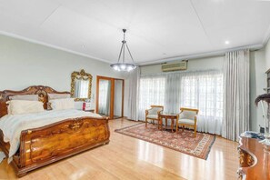 A bedroom with a wooden bed, a chandelier, a large mirror, and a view of the outdoors through the window. - Aaybee Recreational Place (Midrand)
