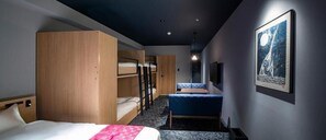 A hotel room with bunk beds, a sofa, a desk, and a wall-mounted TV.