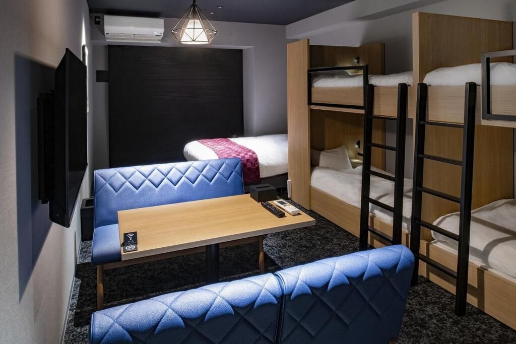 Ein kleines Hotelzimmer mit Etagenbetten, einem Einzelbett, einem Schreibtisch mit Stuhl und einem Fernseher.