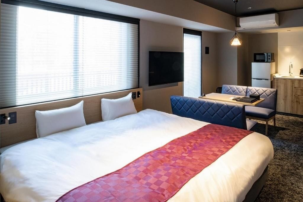 A hotel room with a large bed, a small dining table, a sofa, and a TV mounted on the wall.