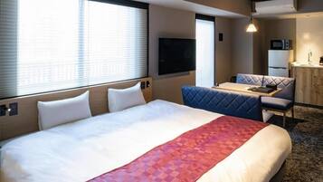 A hotel room with a large bed, a small dining table, a sofa, and a TV mounted on the wall.