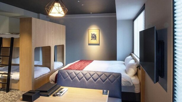 A hotel room with bunk beds, a flat-screen TV, a desk with a chair, and a framed picture on the wall.
