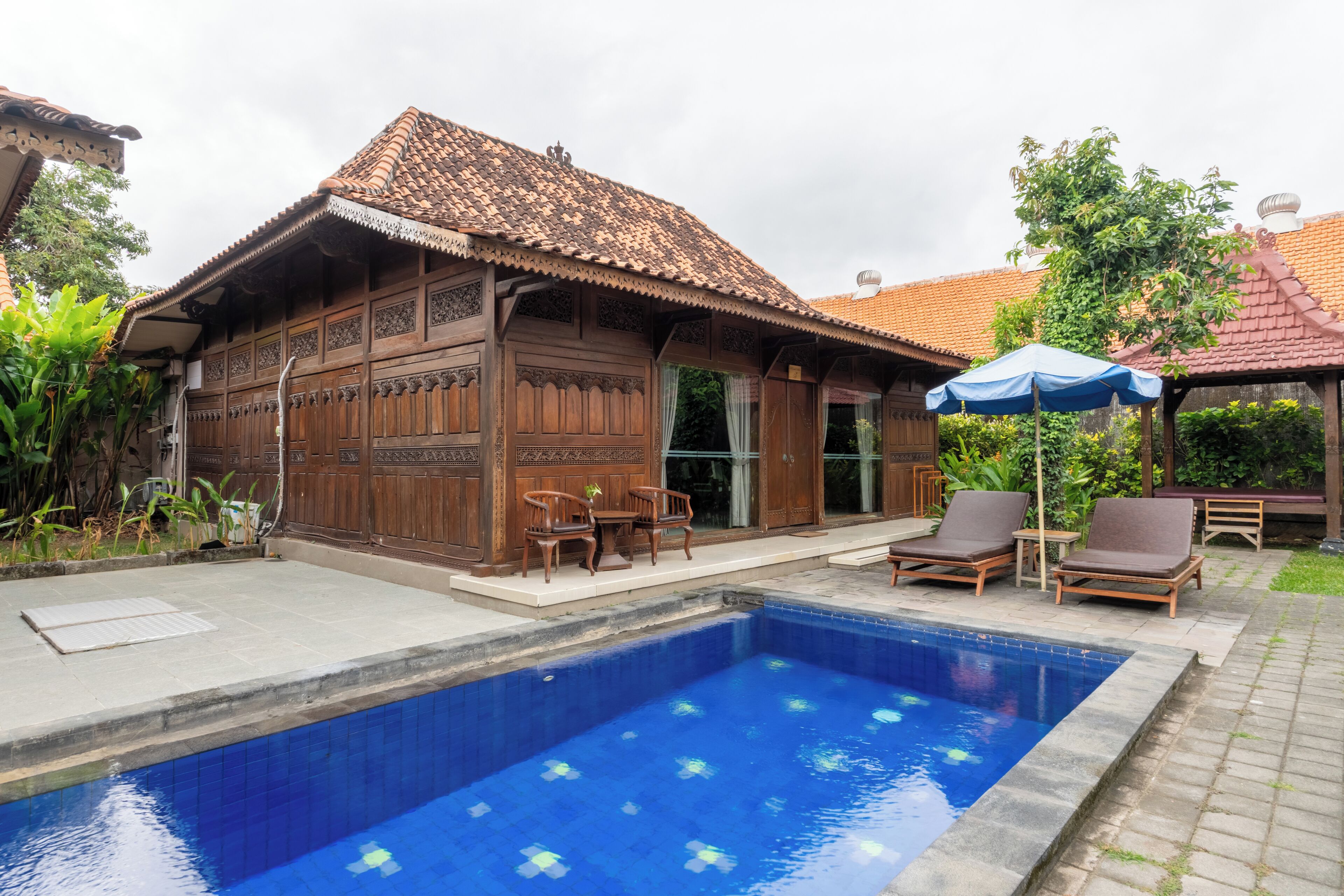 Un edificio de madera tradicional con tejado de baldosas, piscina y mobiliario de exterior.