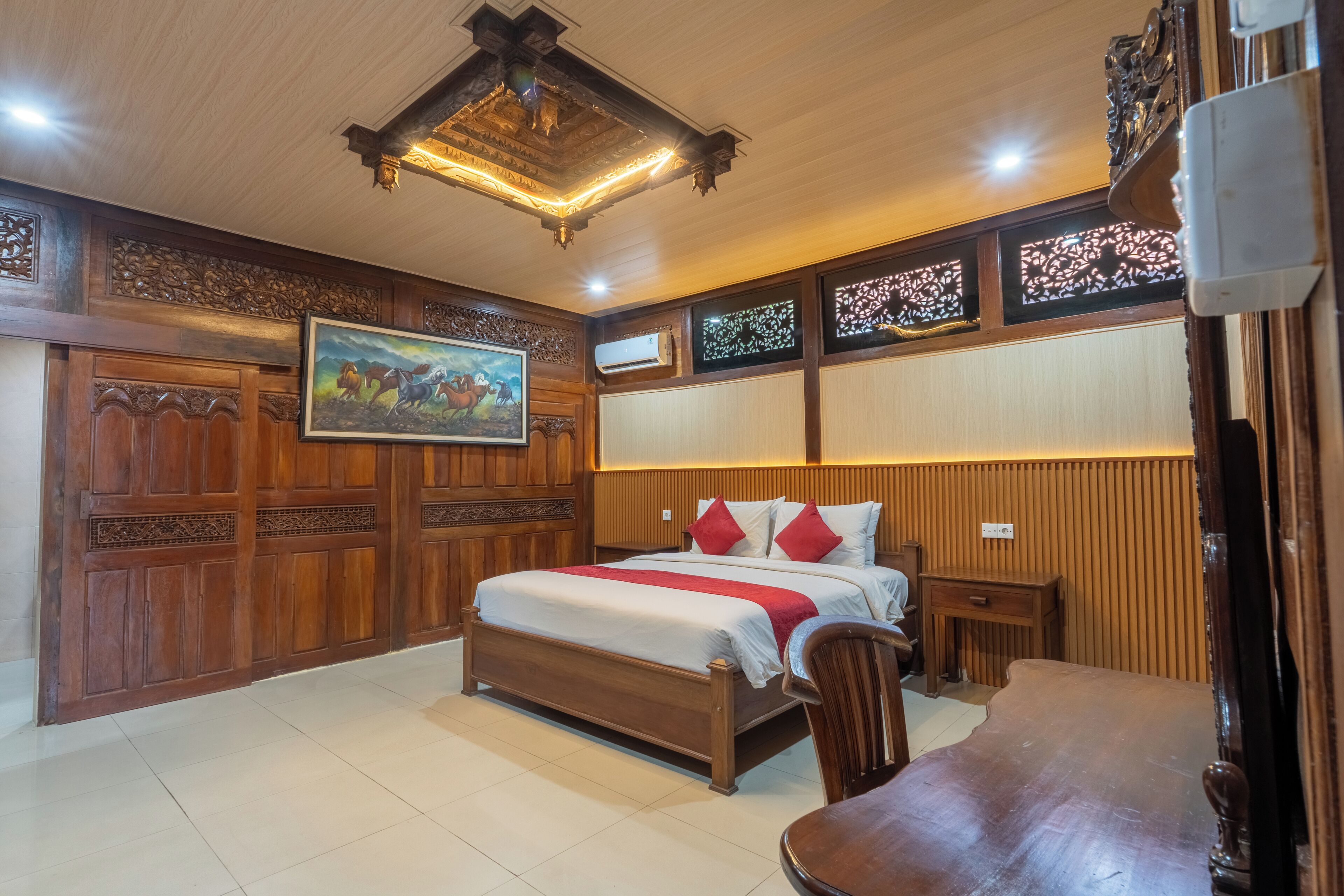 A bedroom with a wooden bed, a painting, a wooden wardrobe, and a ceiling light fixture.