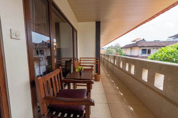 A balcony with a wooden table and chairs, a potted plant, and a view of a residential area.