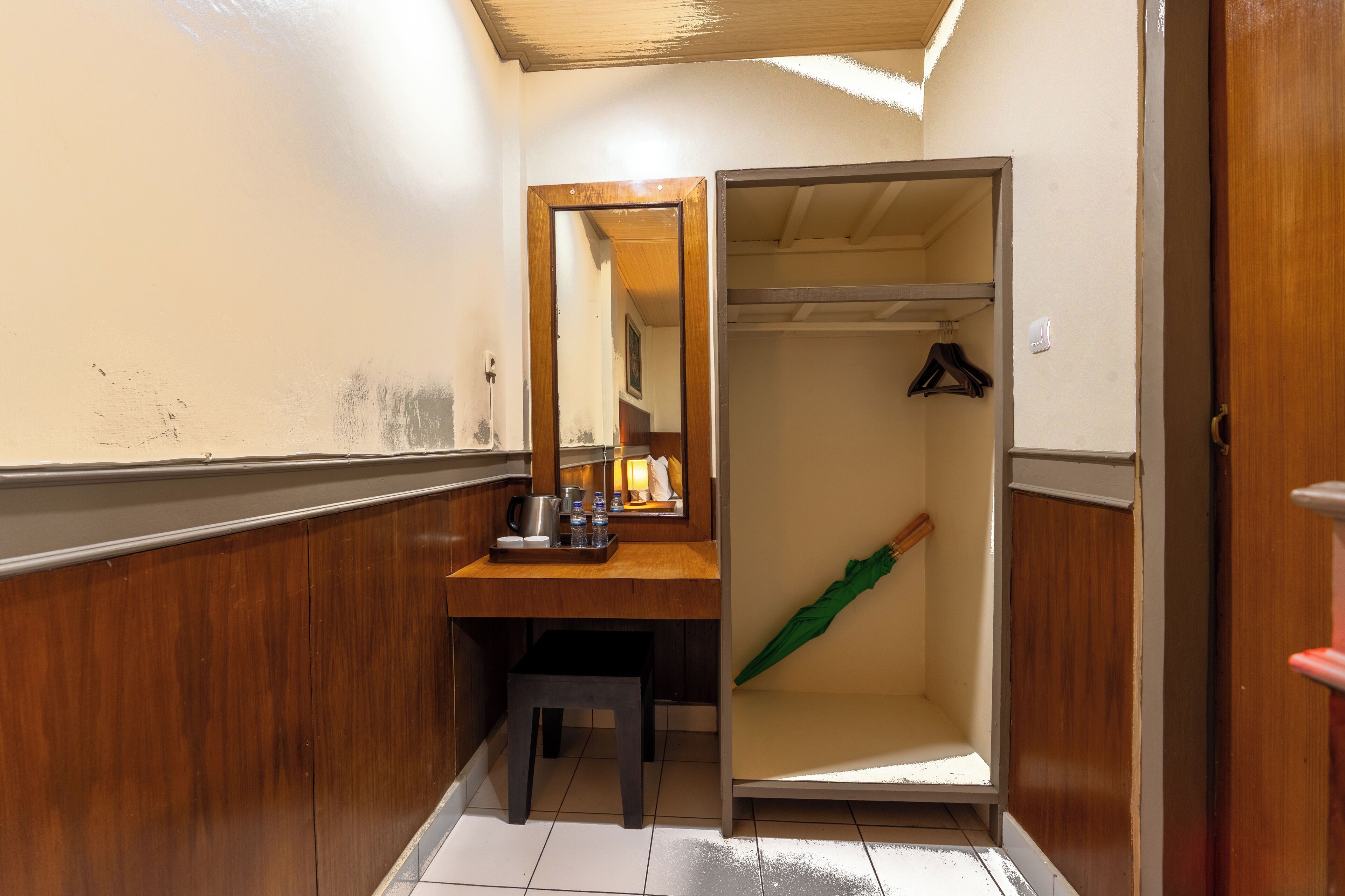 A narrow hallway with a wooden bench, a mirror, and a coat rack with a green umbrella.
