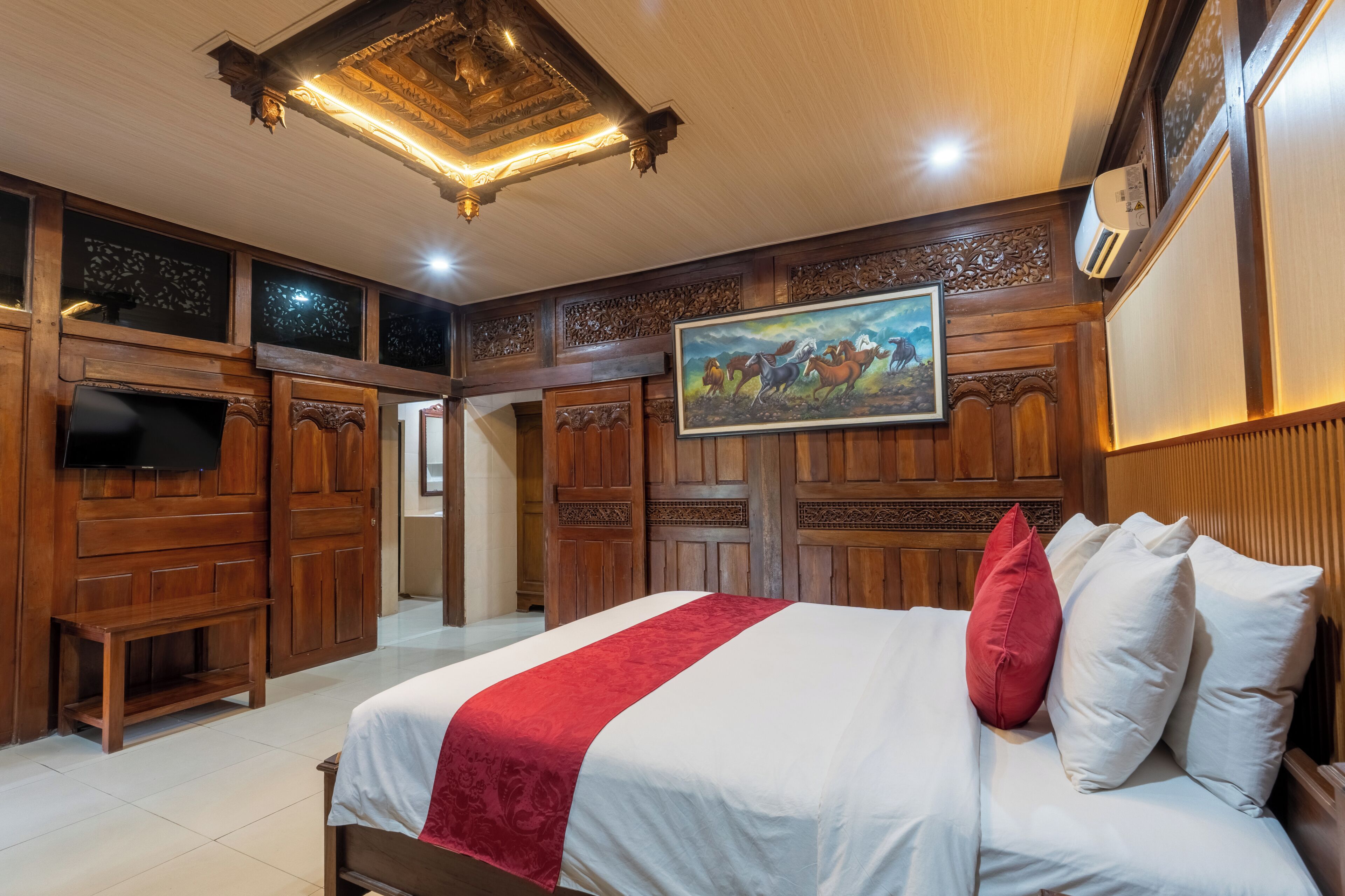 A hotel room with a large bed, wooden paneling, a painting, and a flat-screen TV.