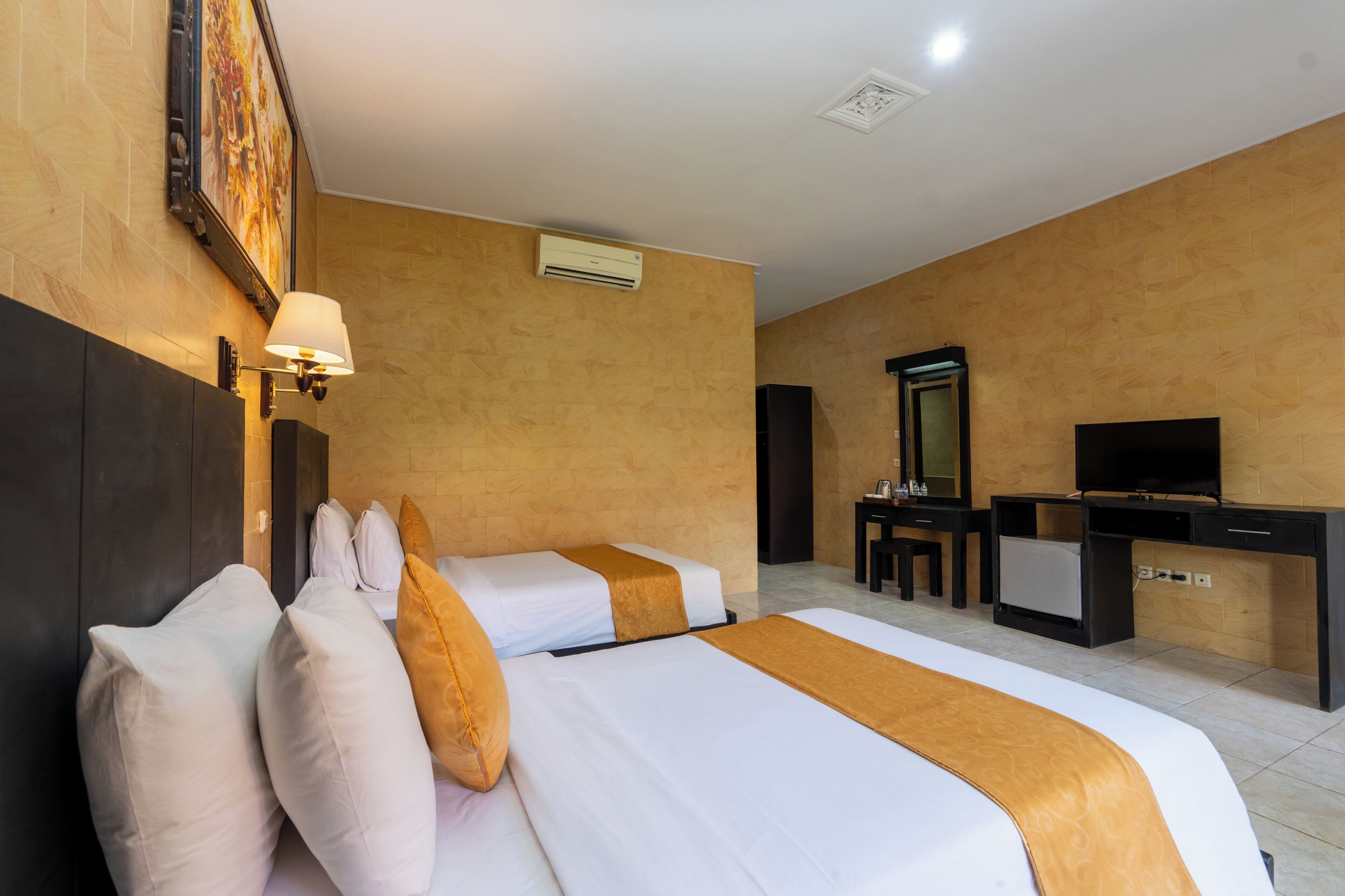 A hotel room with two beds, a desk with a TV, a mirror, and an air conditioning unit on the wall.
