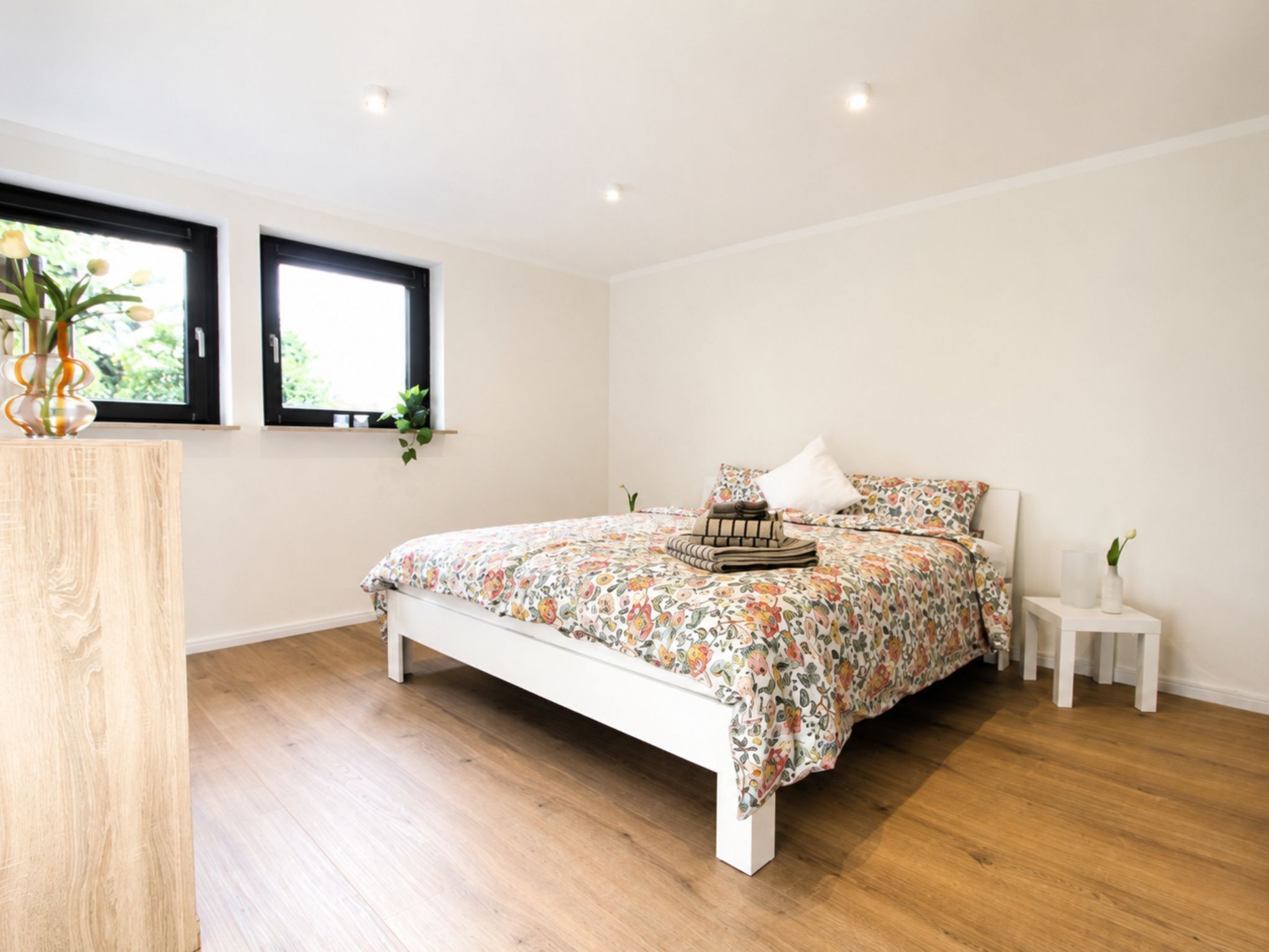 Une chambre à coucher avec un lit, deux fenêtres, une table de chevet et une plante.
