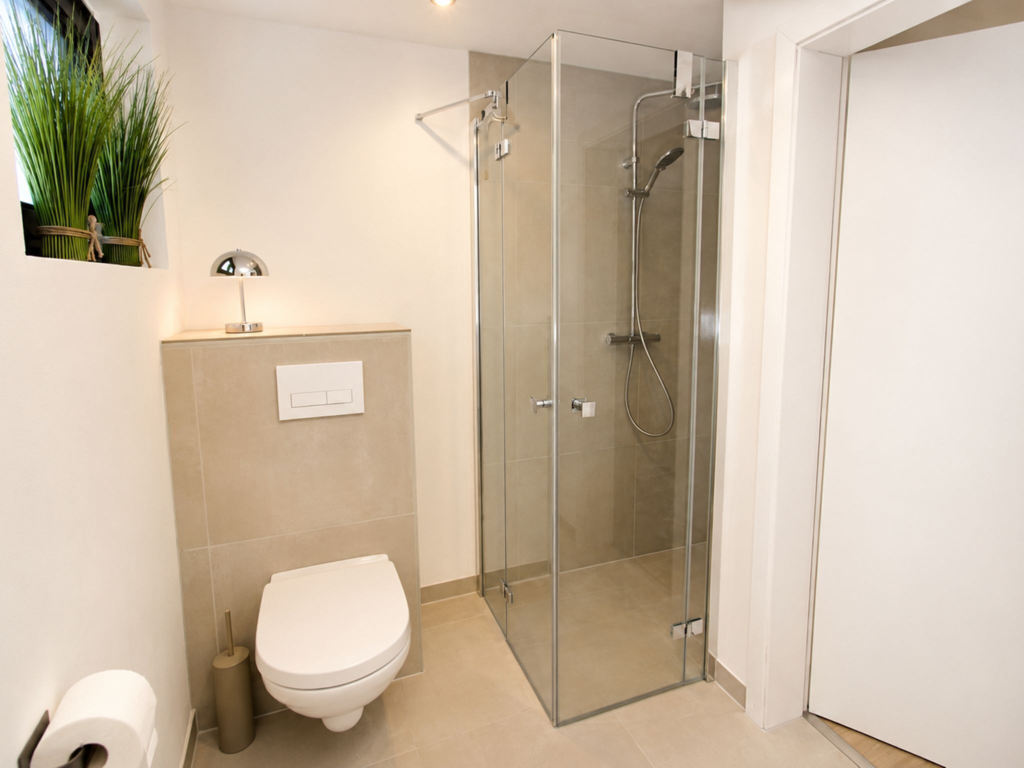 A modern bathroom with a glass-enclosed shower, a toilet, and a small shelf with a lamp.