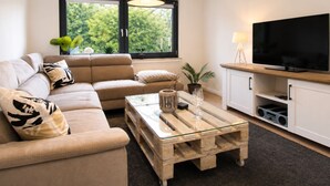 A modern living room with a sofa, coffee table, TV, and windows with a view of greenery. - Herzwerk Schwalenberg by Interhome (Schwalenberg)
