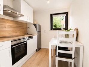 A compact kitchen with white cabinetry, a built-in oven, a stainless steel refrigerator, and a window with a view of greenery. - Herzwerk Schwalenberg by Interhome (Schwalenberg)