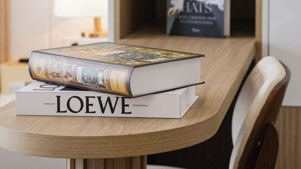 A wooden table with a book titled 'LOEWE Spring Summer' and a lamp on a bedside table. - SOHO Vernal Saigon Apartments (Ho Chi Minh City)