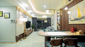 A modern living room with a curved ceiling, a dining area with a marble table, and a large painting of sailboats. - SOHO Vernal Saigon Apartments (Ho Chi Minh City)
