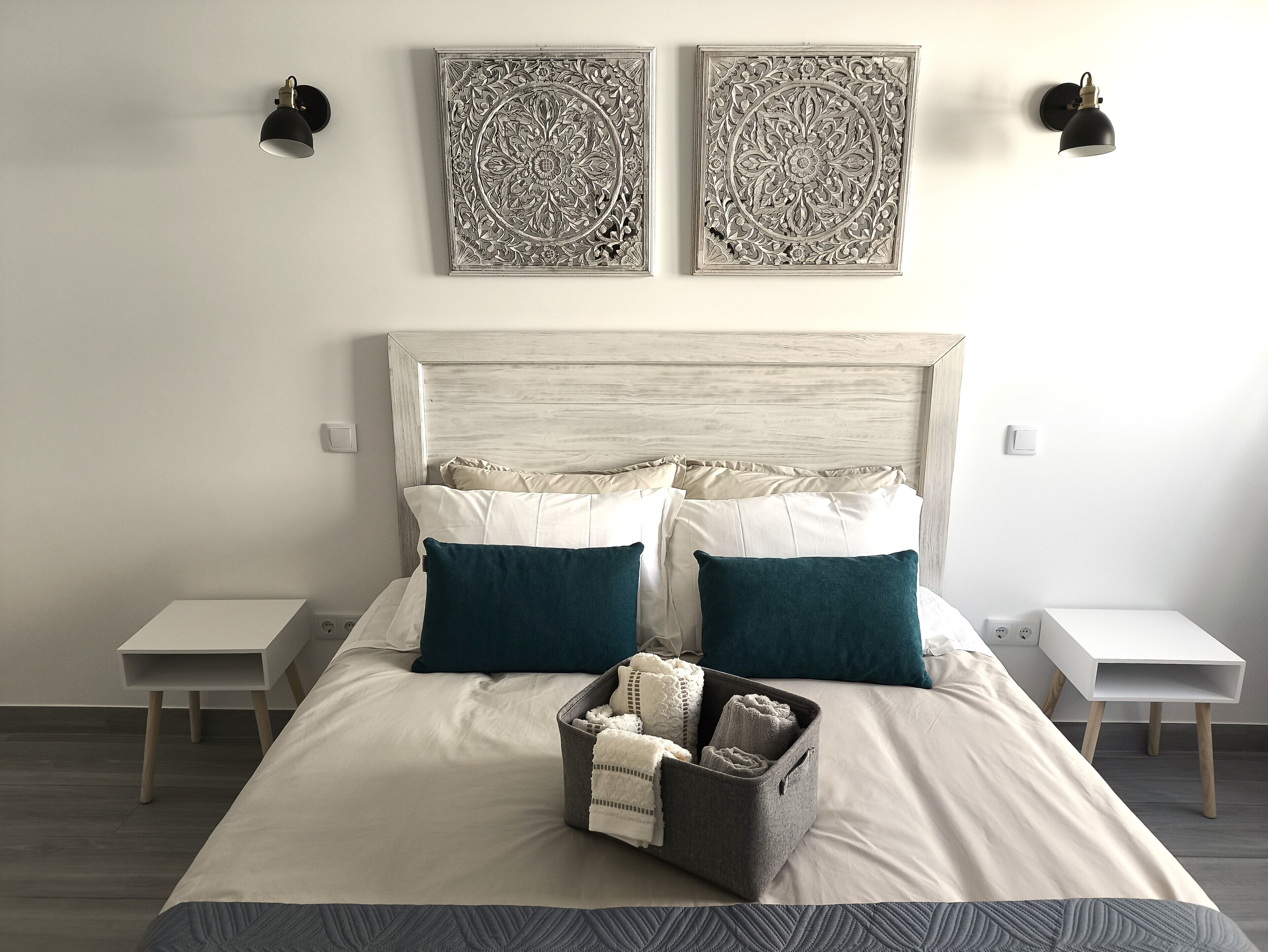 Un lit bien fait, avec une tête de lit, deux tables de chevet et une lampe fixée au mur.