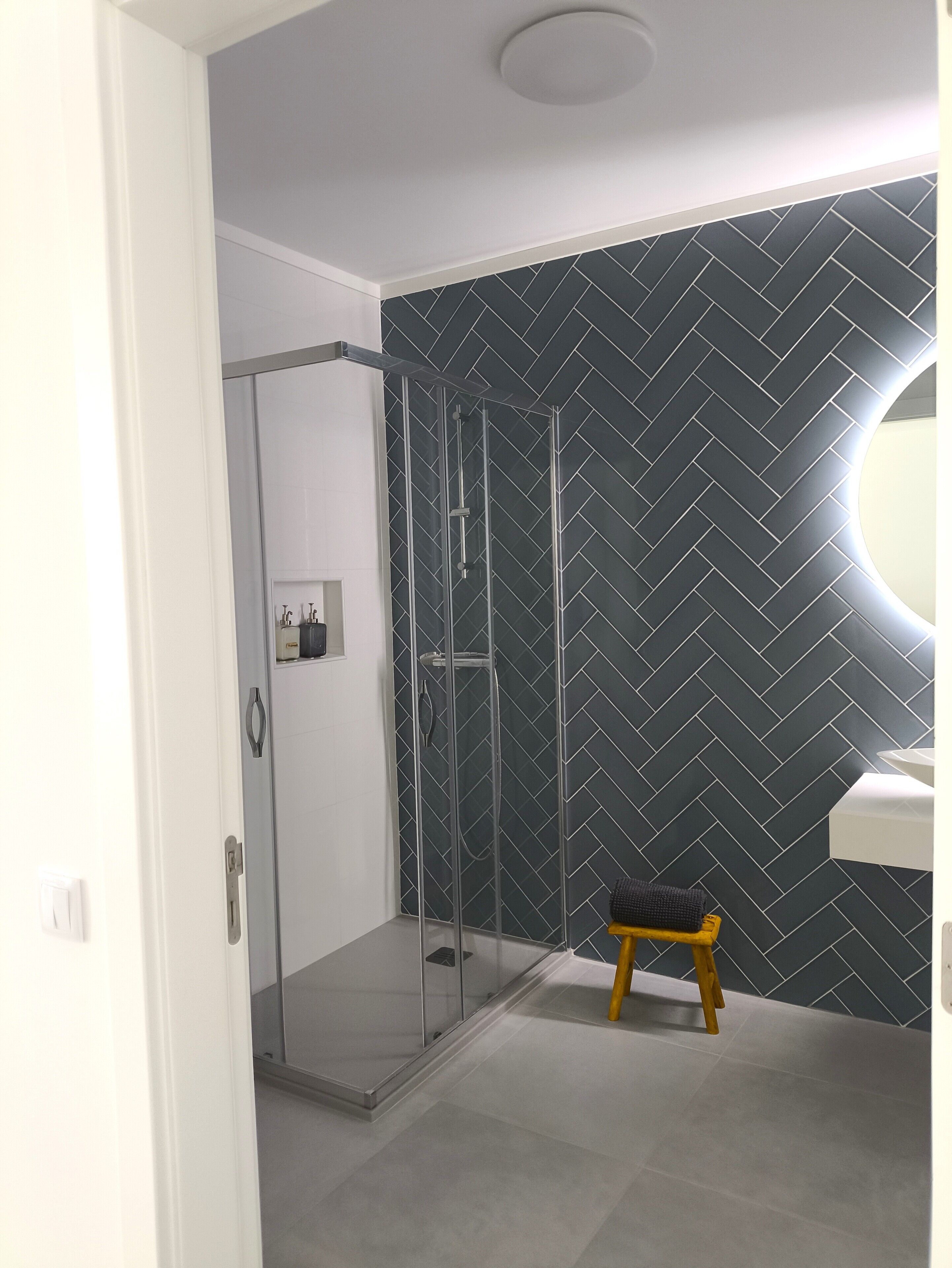 Ein modernes Badezimmer mit Duschkabine aus Glas, Wand in Fischgrätmuster und einer kleinen Hocker.