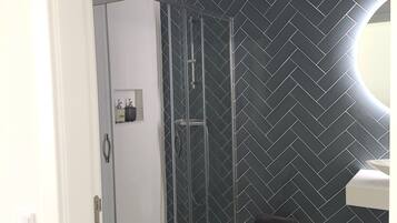 Ein modernes Badezimmer mit Duschkabine aus Glas, Wand in Fischgrätmuster und einer kleinen Hocker.