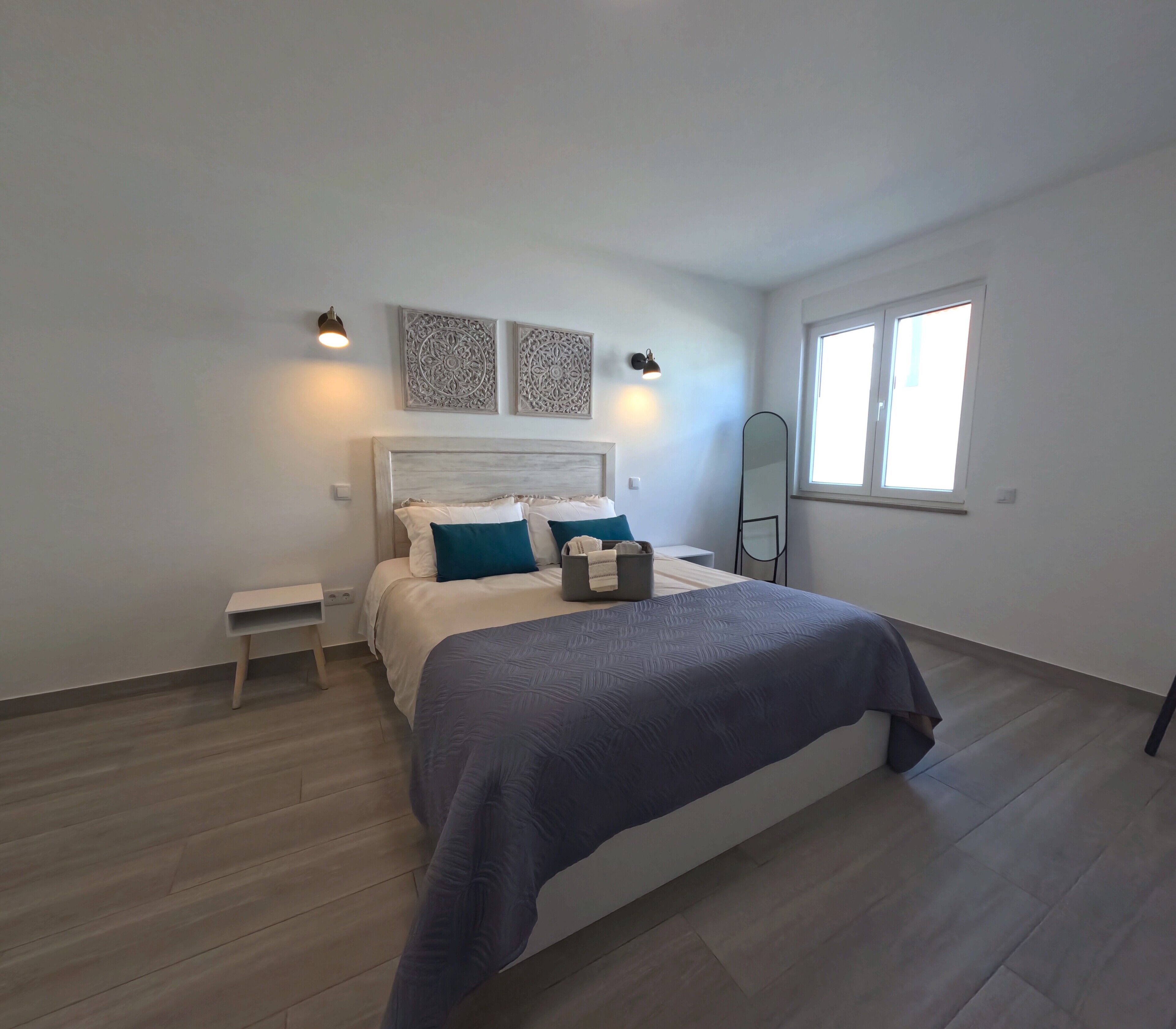 Une chambre à coucher comprenant un lit, des tables de chevet, une commode, des lampes fixées au mur et une fenêtre.