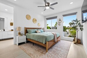 Ein modernes Schlafzimmer mit einem Bett, Nachttischen, einem Deckenventilator und großen Fenstern.
