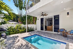 Ein moderner Poolbereich im Freien mit einem klaren, blauen Pool, einem Deckenventilator und einer Terrasse mit Stühlen.
