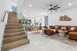 A modern interior with a staircase, a dining area, a living room with a sofa, and a ceiling fan. - Private Pool + 4 Ensuite Baths | Victoria Park + Las Olas | Park & Palm (Fort Lauderdale)