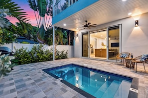 A modern outdoor pool area with a clear blue pool, a ceiling fan, and a dining area with wicker furniture. - Private Pool + 4 Ensuite Baths | Victoria Park + Las Olas | Park & Palm (Fort Lauderdale)