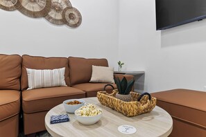Ein modernes Wohnzimmer mit einem braunen Ledersofa, einem runden Couchtisch mit Snacks und einem flachbildfernseher an der Wand.