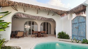 A poolside area with a dining set, a blue door, and a thatched roof. - Villa Harmony (Badung)