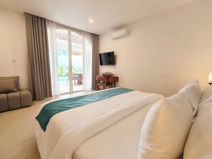 A hotel room with a bed, a sofa, a TV, and a sliding glass door to a pool area. - Villa Harmony (Badung)