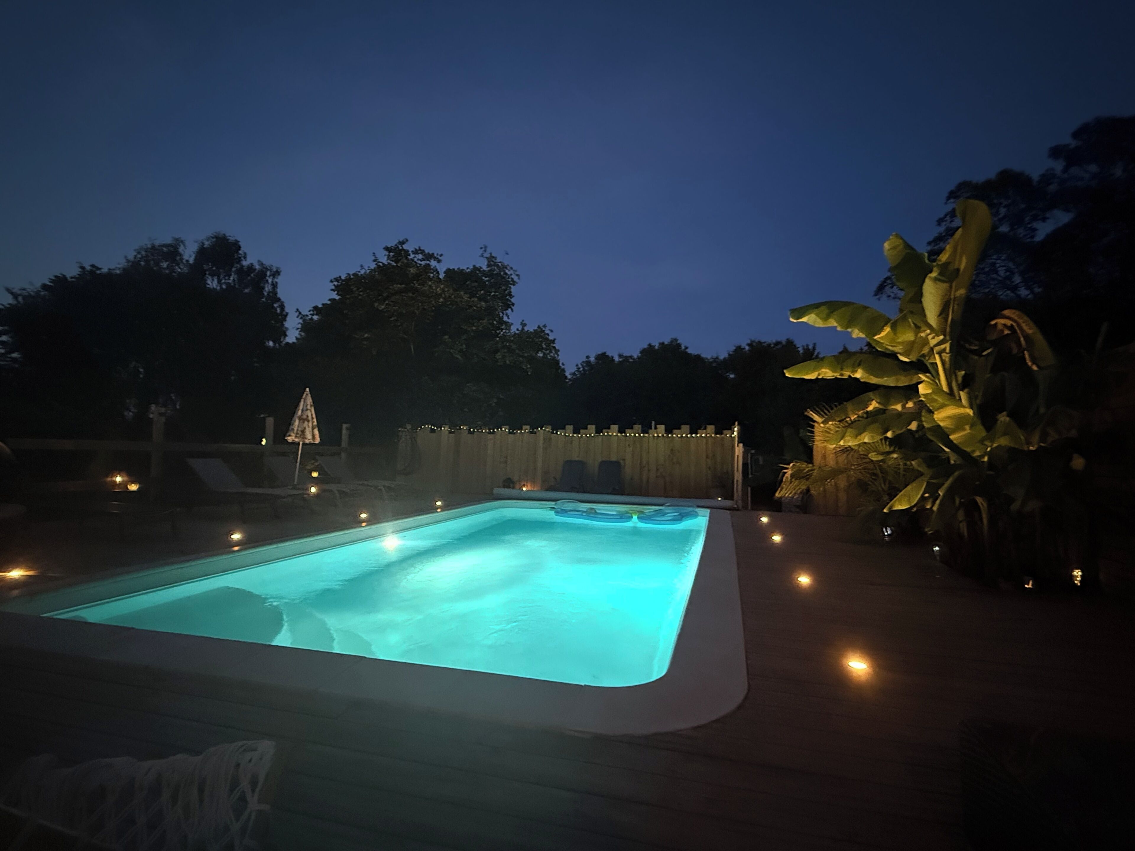 A rectangular swimming pool with a light blue tint, surrounded by a wooden deck and a wooden fence.