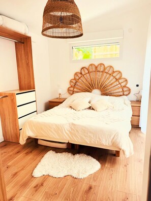 A bedroom with a bed, a wicker ceiling light, a window, and a wooden floor.