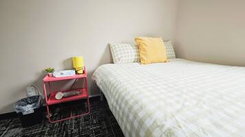 A hotel room with a bed, a nightstand, a lamp, a power outlet, and a trash bin.