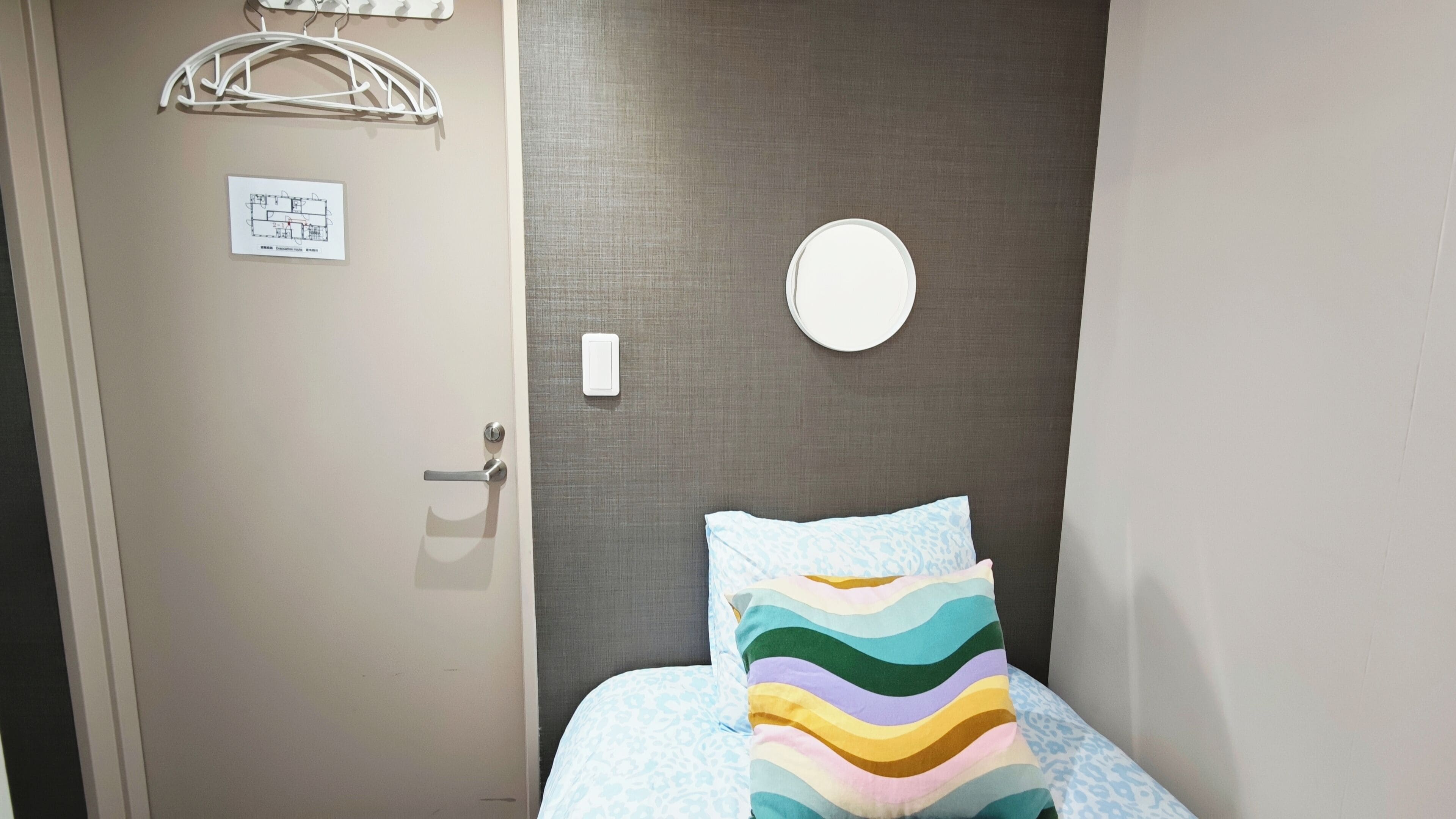 Une chambre d’hôtel avec un lit, une porte, un luminaire fixé au mur et un miroir fixé au mur.