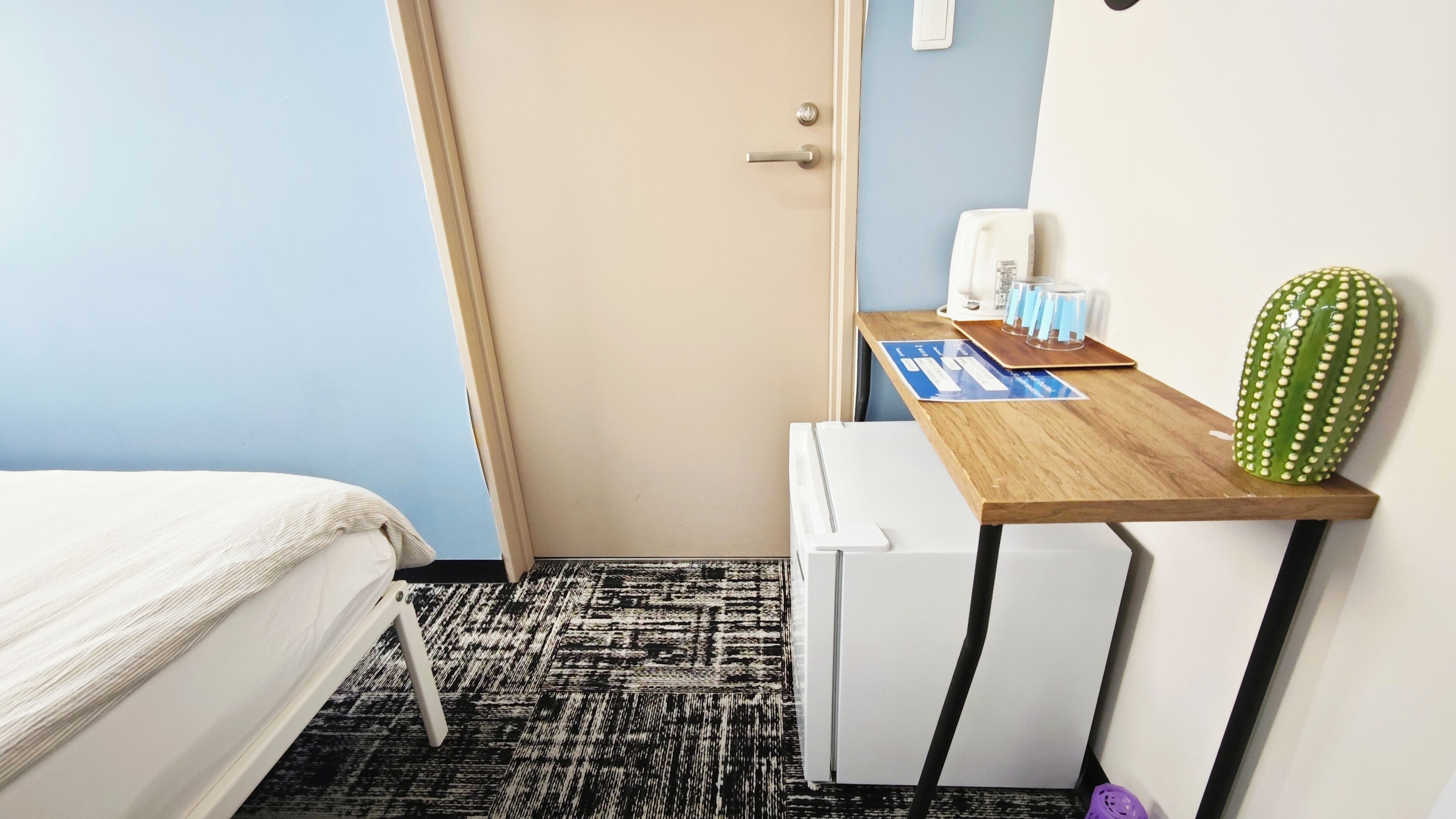 Une chambre d’hôtel avec un lit, un bureau orné d’un cactus, une machine à café et un petit radiateur.