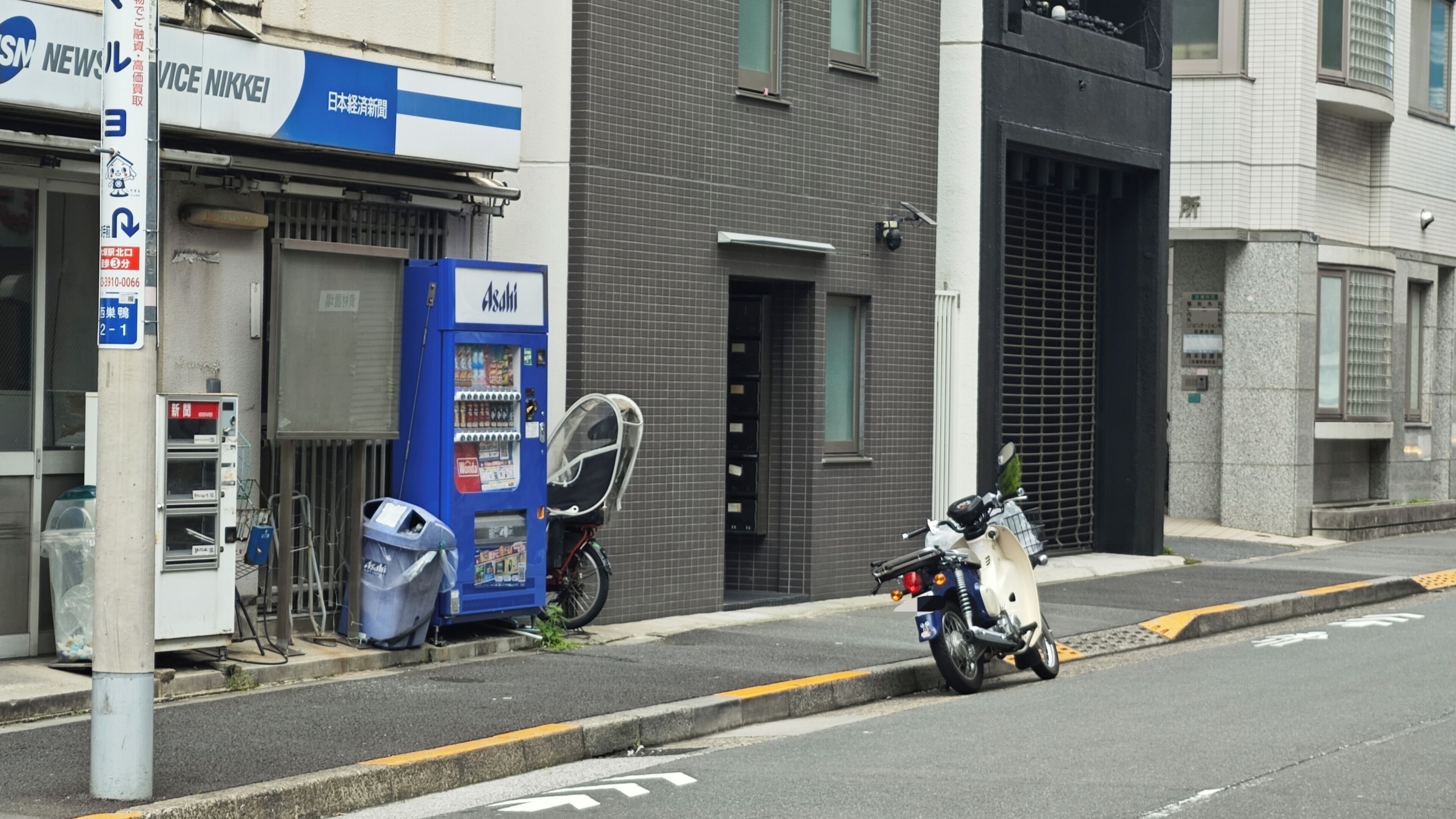 A street with a blue vending machine, a motorcycle, and a building with a sign that reads 'NIKKEI'.